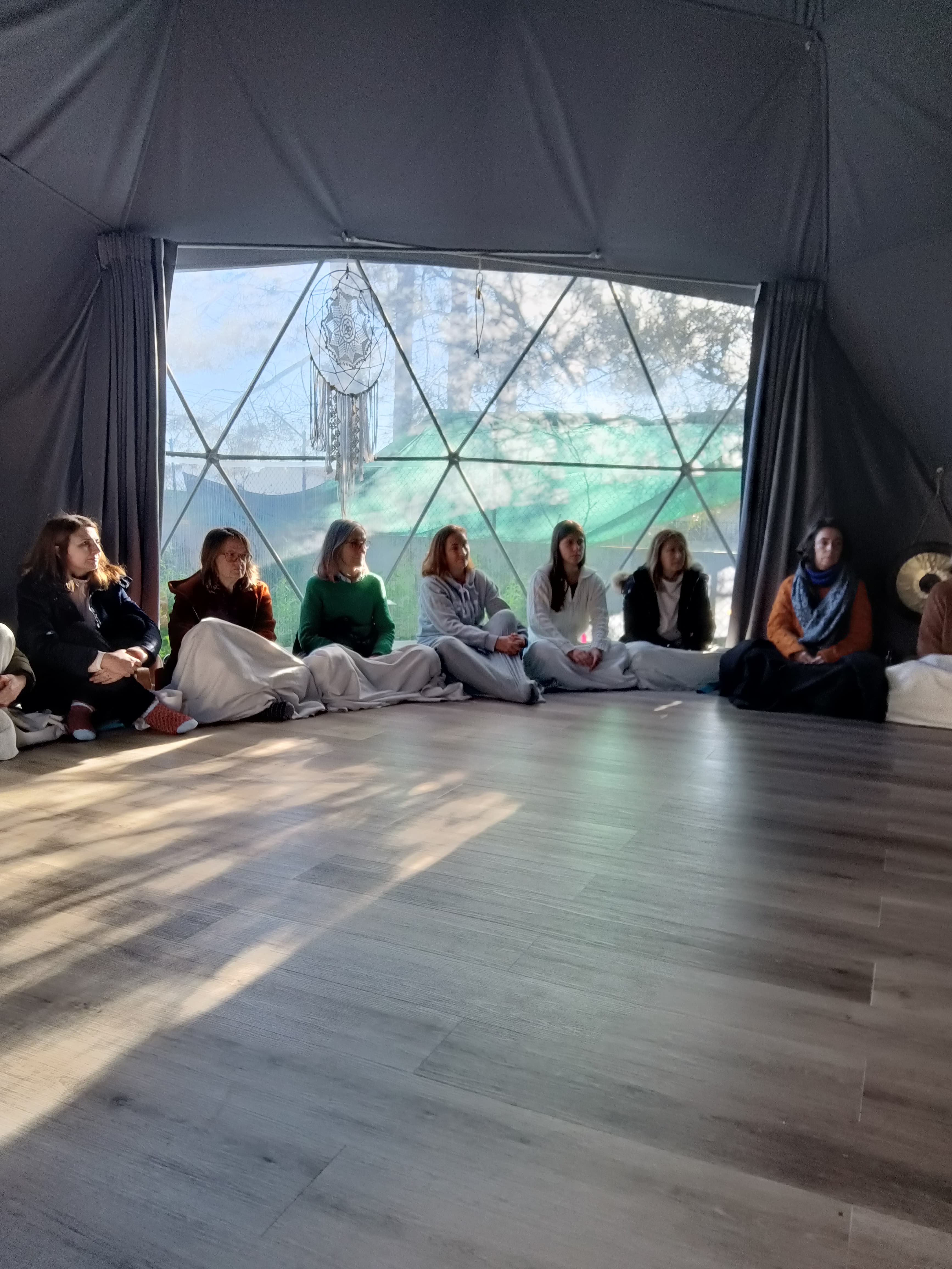 Mulher sentada em meditação, de olhos fechados, num quarto claro