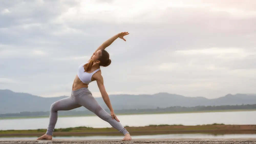 Mulher em postura de yoga ao ar livre, junto à água, ao nascer do sol